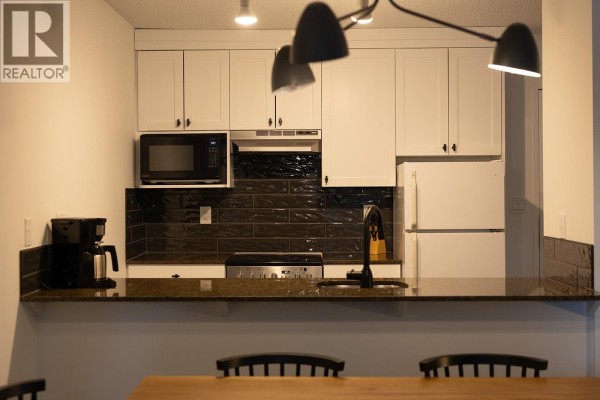 Kitchen with white cabinetry, black backsplash, stainless steel appliances, and a breakfast bar. - 208 4200 Whistler Way, Whistler