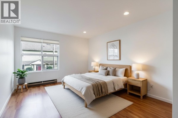 Bedroom with queen bed, nightstands, and a large window overlooking houses and trees. - 208 4989 47 Avenue, Ladner