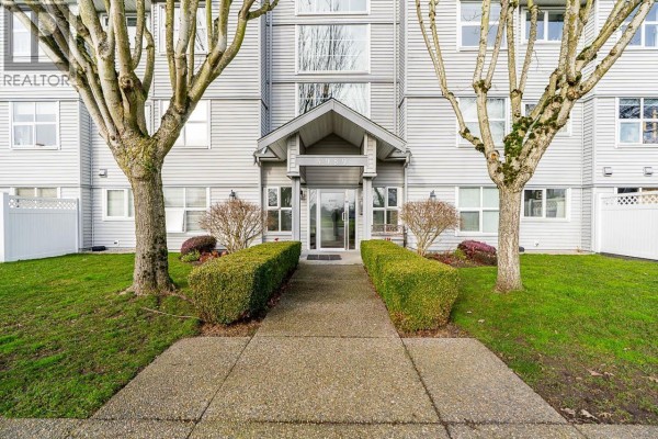 Living room with fireplace, large windows, and sliding glass doors leading to a balcony. - 208 4989 47 Avenue, Ladner