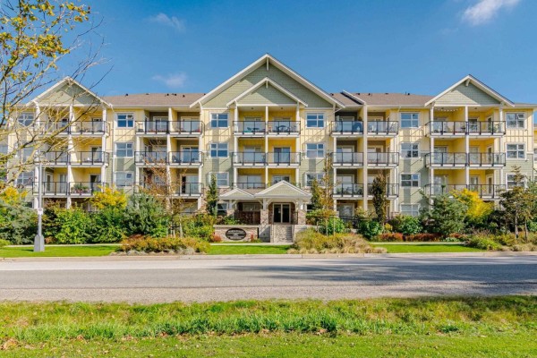 Exterior of a multi-story apartment building with yellow and green siding and many balconies. - 208 5020 221a Street, Langley