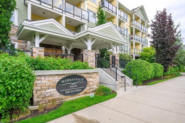 Entrance to a brick and stone apartment building with a covered entryway and landscaping. - 208 5020 221a Street, Langley