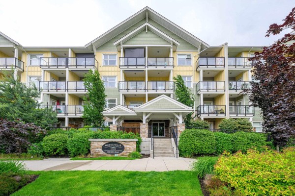 Exterior view of an apartment building featuring yellow siding, green accents, and balconies. - 208 5020 221a Street, Langley