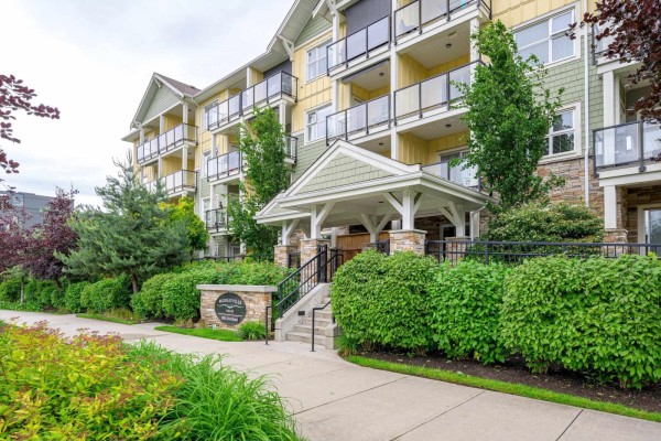 Walkway leading to the entrance of an apartment building with stone accents and lush landscaping. - 208 5020 221a Street, Langley