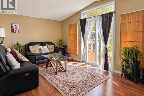 Living room with tan walls, vaulted ceiling, dark leather couch, glass coffee table, and sliding doors to deck. - 208 Activa Avenue, Kitchener