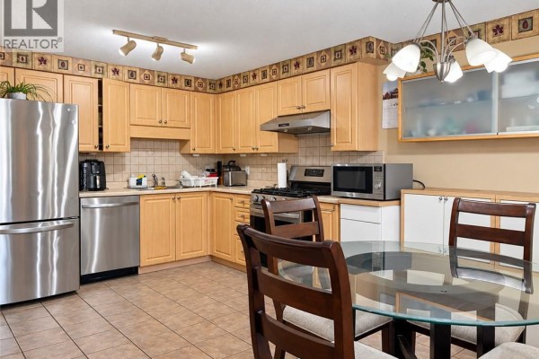 Kitchen with light wood cabinets, stainless steel appliances, tile floor, and a glass dining table. - 208 Activa Avenue, Kitchener