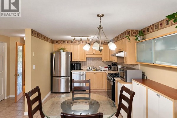 View of the kitchen area with light wood cabinets, stainless steel refrigerator, and a round glass dining table. - 208 Activa Avenue, Kitchener