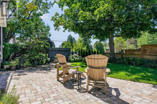 Back exterior of a red brick house with a patio, lawn, and detached garage with glass doors. - 208 Albert Street, Cobourg