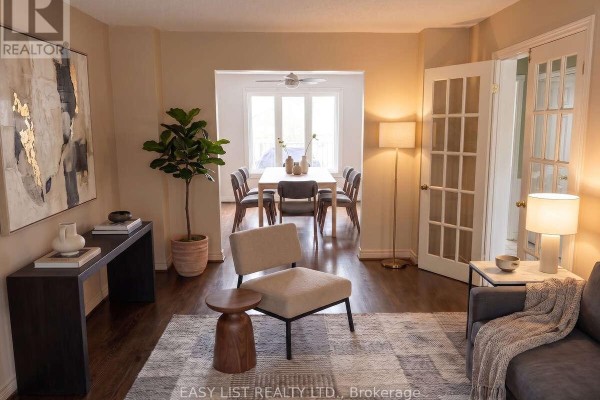 Living room with dark hardwood floors, beige sofa, and dining area visible through doorway. - 208 Anastasia Terrace, Mississauga
