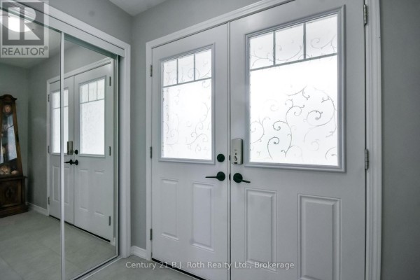 Interior view of the front entryway with double doors, frosted glass panels, and a mirrored closet. - 208 Diana Drive, Orillia