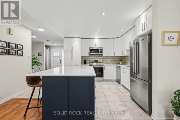 Open-concept kitchen with white cabinets, stainless steel appliances, and a navy island with bar stools. - 208 Jamieson Street, Mississippi Mills
