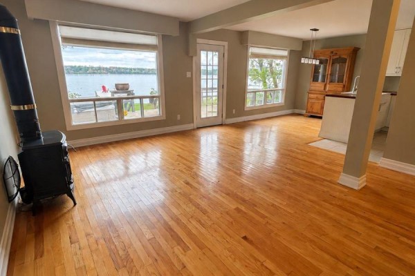 Spacious living area with hardwood floors, a wood stove, and water views through windows. - 208 Kempview Lane, Barrie
