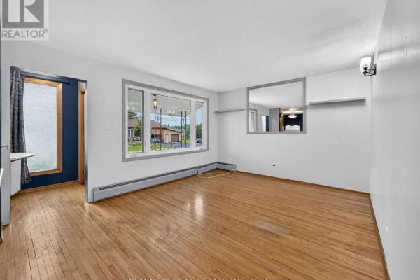 Living room with hardwood floors, a large window, and white walls with a large mirror. - 208 Marion Street, Iroquois Falls