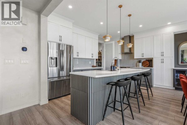 Living room and kitchen area with a fireplace, island seating, and white cabinetry. - 208 Osborne Green Sw, Airdrie