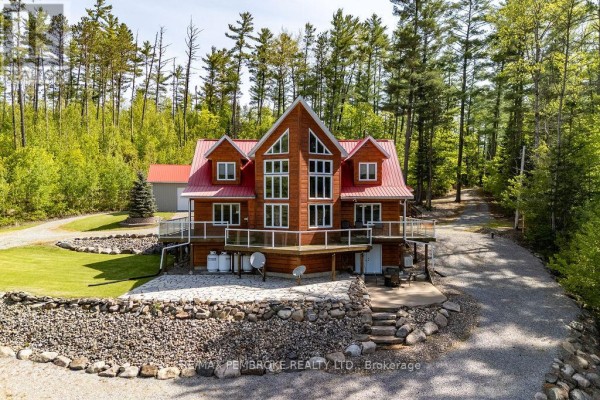 Front view of a two-story wooden house featuring a prominent glass facade and a wide wooden deck. - 208 Red Fox Trail, Head, Clara And Maria
