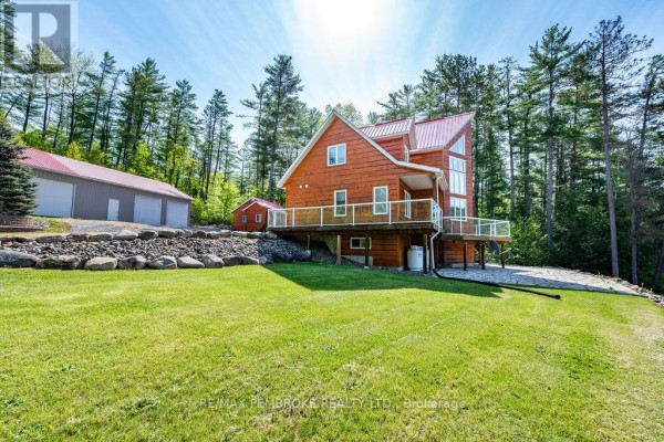 Side view of a wooden house with a red metal roof, showing a large deck and a detached garage. - 208 Red Fox Trail, Head, Clara And Maria