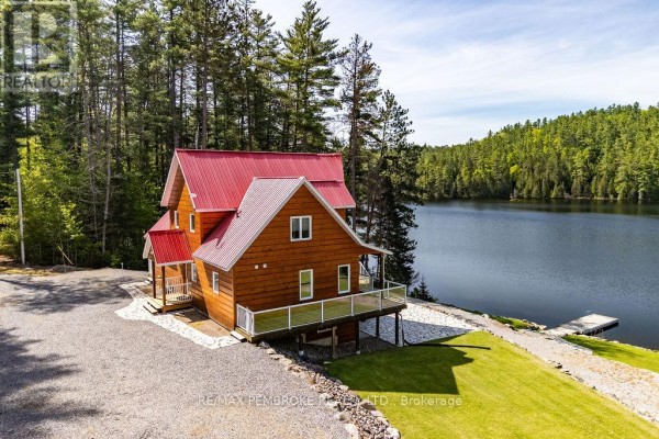 View of a wooden house with a red roof situated beside a calm lake with a small dock. - 208 Red Fox Trail, Head, Clara And Maria