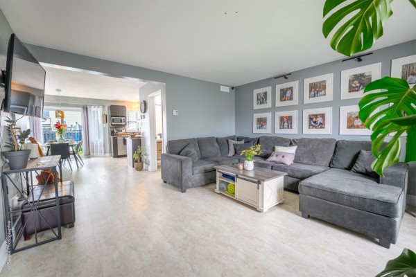Living room with grey walls, a large sectional sofa, a coffee table, and a wall of framed photos. - 208 Rue Paul-laframboise, Gatineau
