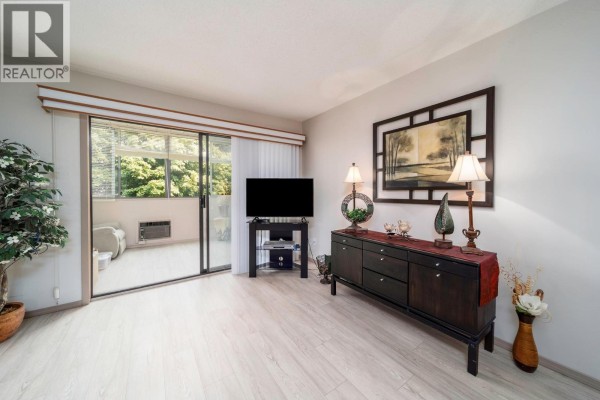 Living room with dark wood buffet, television, and sliding glass door to balcony. - 2085 Gordon Drive Unit# 211, Kelowna