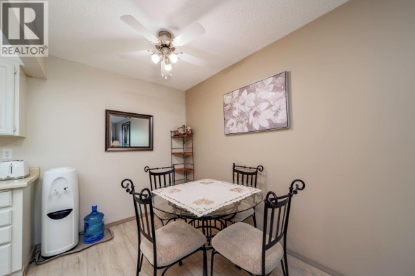 Dining area with glass-top table, four chairs, and water cooler next to kitchen. - 2085 Gordon Drive Unit# 211, Kelowna