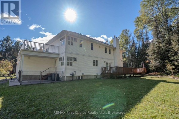 Rear view of a white house with a large deck and wooden patio with stairs. - 2086 Granite Road, Thunder Bay
