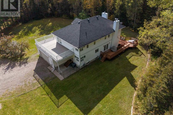 Aerial view of a white house with a large deck and attached garage in a wooded area. - 2086 Granite Road, Thunder Bay