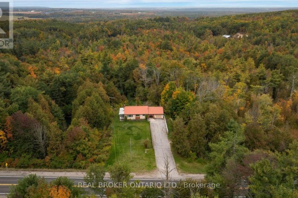 Aerial view showing a home nestled amongst a vast expanse of autumn-colored trees and rolling hills. - 2086 Penetanguishene Road, Springwater