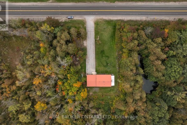 Direct overhead aerial view of the bungalow with an orange roof, surrounded by trees and a pond. - 2086 Penetanguishene Road, Springwater
