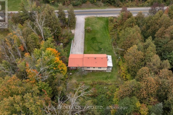 Aerial view of the bungalow from the side, showing the orange roof, white trim, and the surrounding wooded lot. - 2086 Penetanguishene Road, Springwater