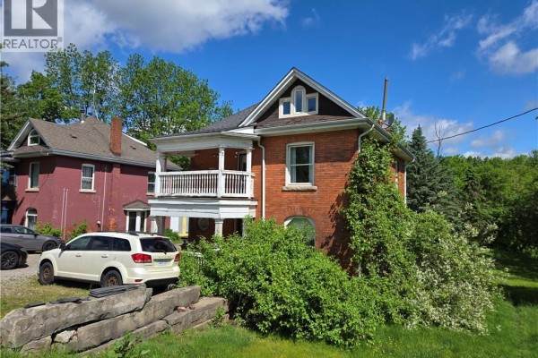 Front and side view of a red brick house with white trim and overgrown greenery. - 2087 Governors Road, Copetown