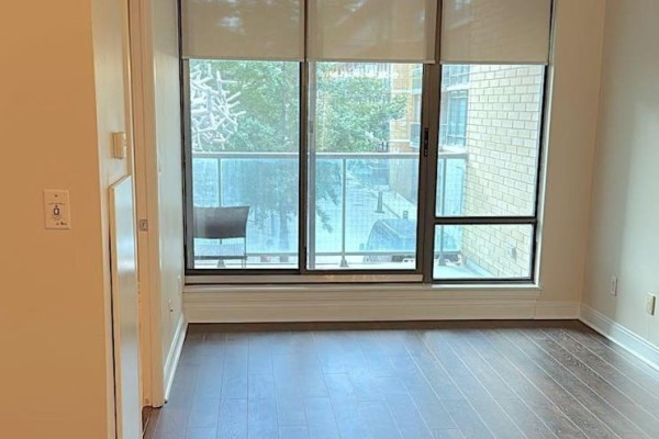 Living area with dark hardwood floors, beige walls, and large windows overlooking the city street. - 209 - 18 Yorkville Avenue, Toronto