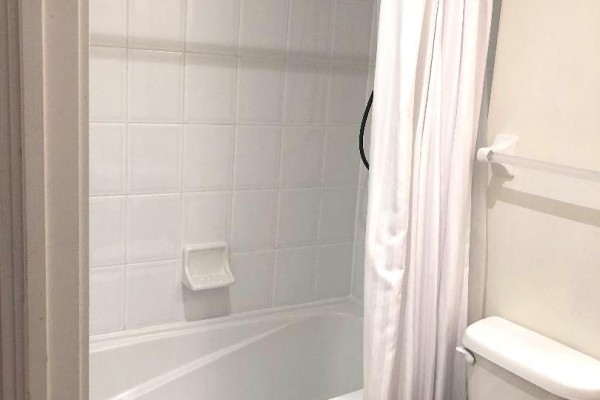 Bathroom with white tiled walls, a white bathtub, a white toilet, and a white shower curtain. - 209 - 18 Yorkville Avenue, Toronto