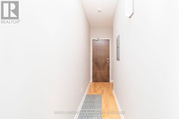 Hallway with light grey walls, wood floor, and a brown apartment door. - 209 - 180 York Street, Ottawa