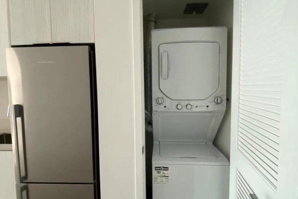 Stacked white washer and dryer unit located next to the stainless steel refrigerator. - 209 - 25 Richmond Street E, Toronto