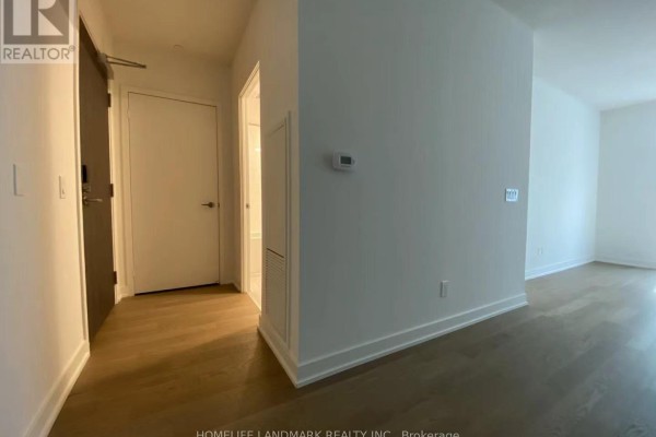 Hallway leading to the front door and bathroom, with neutral walls and hardwood flooring. - 209 - 25 Richmond Street E, Toronto