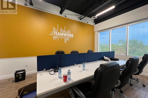 Conference room with large table, executive chairs, two accent chairs, and a textured stone accent wall. - 209 - 3485 Rebecca Street, Oakville