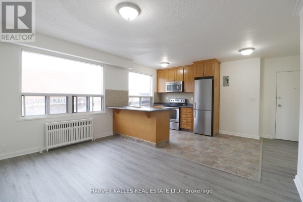 Kitchen and living area with light wood cabinets and stainless steel appliances. - 209 - 500 Gilbert Avenue, Toronto