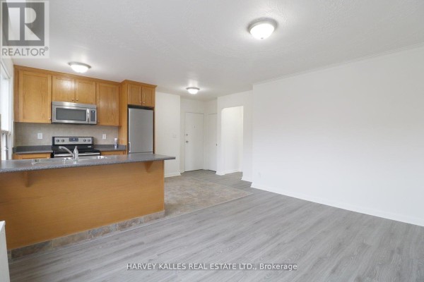 Open-concept living and kitchen area with light wood cabinets and grey flooring. - 209 - 500 Gilbert Avenue, Toronto
