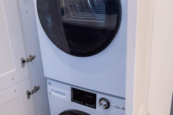 White stacked washer and dryer inside a closet with wooden doors. - 6479 Montrose Road, Niagara Falls