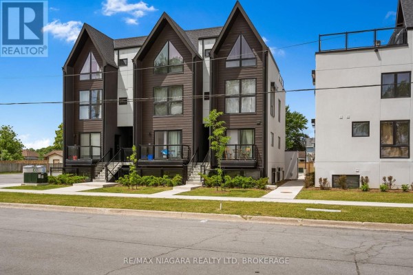 Close-up exterior view of a modern townhouse complex showing dark brown siding and windows. - 209 - 7277 Wilson Crescent, Niagara Falls