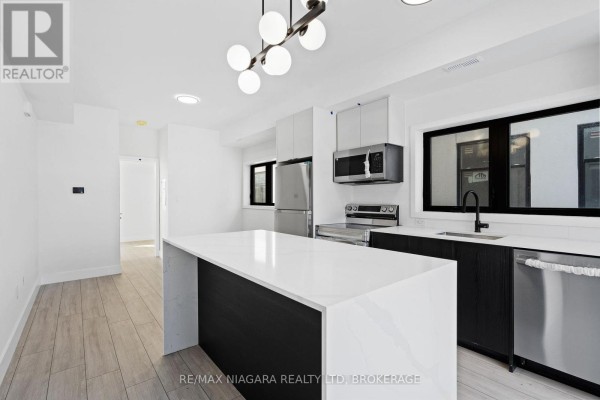 Modern kitchen with white quartz island, stainless steel appliances, and dark lower cabinets. - 209 - 7277 Wilson Crescent, Niagara Falls