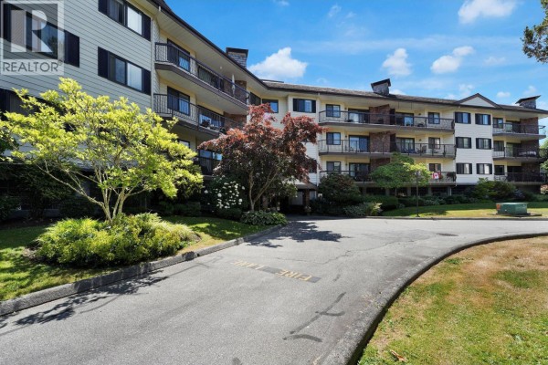 Exterior of the apartment building with balconies and lush green trees. - 209 10220 Ryan Road, Richmond