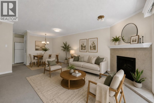 Living room featuring a fireplace, beige carpet, and view of trees. - 209 10220 Ryan Road, Richmond