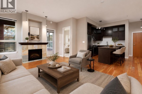Living room featuring a sofa, armchair, fireplace, and large windows. - 209 240 Salter Street, New Westminster