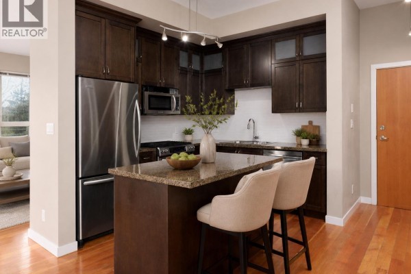 View of the kitchen island with bar stools and surrounding dark wood cabinetry. - 209 240 Salter Street, New Westminster