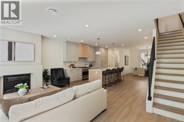 Kitchen island with light grey cabinets, waterfall countertop, and bar stools. - 209 2770 Vantilburg Cres, Langford