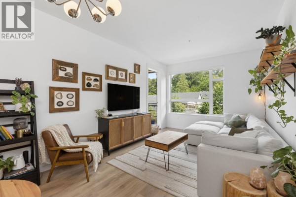 Living room with white sectional sofa, coffee table, media console, armchair, and large window. - 209 715 W 15th Street, North Vancouver