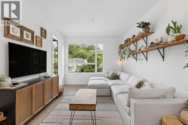 Living room with white sectional sofa, media console, coffee table, and view through window. - 209 715 W 15th Street, North Vancouver