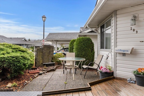 Front porch with outdoor seating, table, and planters, adjacent to duplex exterior. - 209 7610 Evans Road, Sardis West Vedder, Chilliwack
