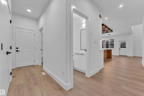 Hallway leading to kitchen area with light wood flooring and white walls. - 209 Basin Co, Leduc
