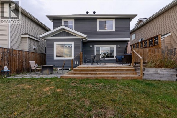 Backyard view of a dark grey house with a wooden deck and lawn furniture. - 209 Blackburn Drive, Fort Mcmurray